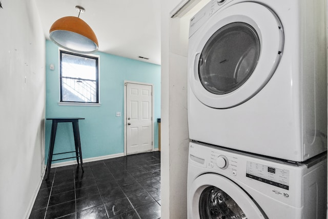 washroom with stacked washing maching and dryer and dark tile patterned floors