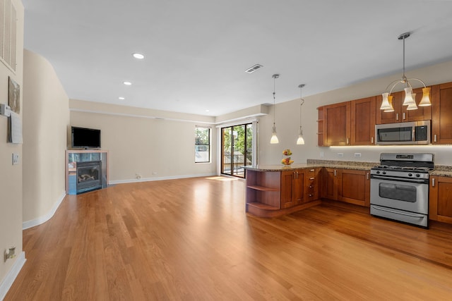 kitchen with hanging light fixtures, light hardwood / wood-style flooring, light stone counters, stainless steel appliances, and kitchen peninsula