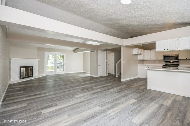 unfurnished living room with a textured ceiling, light wood-type flooring, and a brick fireplace