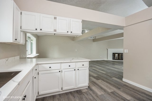 kitchen featuring white cabinetry, dark hardwood / wood-style flooring, kitchen peninsula, and a brick fireplace