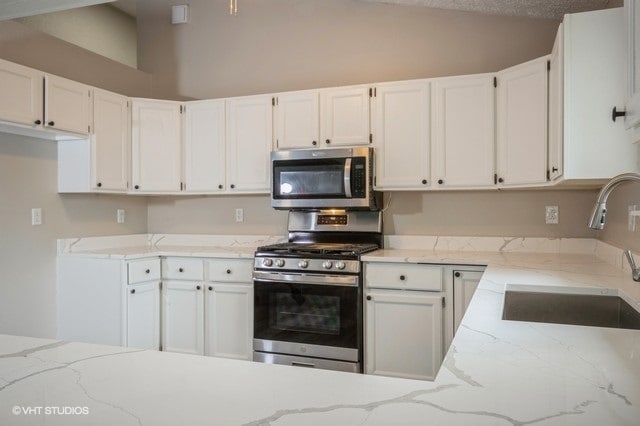 kitchen featuring stainless steel appliances, sink, light stone countertops, and white cabinetry