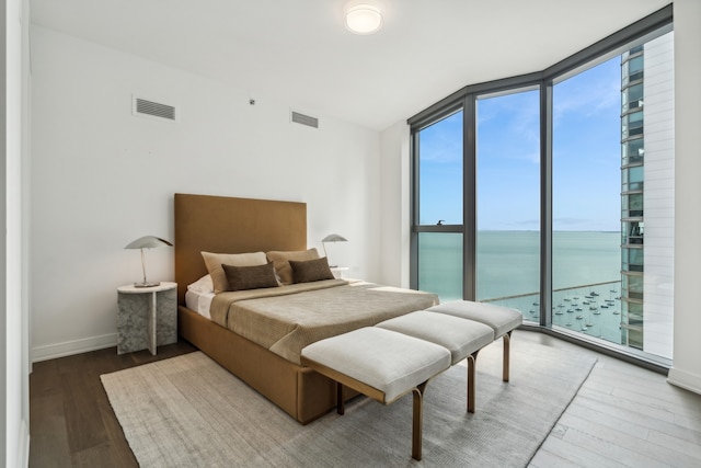 bedroom with a wall of windows, a water view, hardwood / wood-style floors, and access to exterior