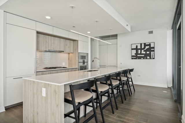 kitchen featuring hanging light fixtures, dark wood-type flooring, stainless steel gas cooktop, a breakfast bar area, and a center island with sink