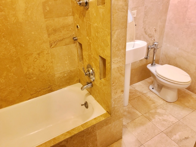 bathroom featuring tile patterned flooring, tile walls, toilet, and tiled shower / bath combo