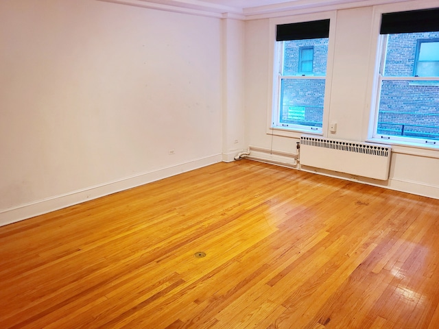 empty room featuring ornamental molding, radiator heating unit, and light hardwood / wood-style flooring