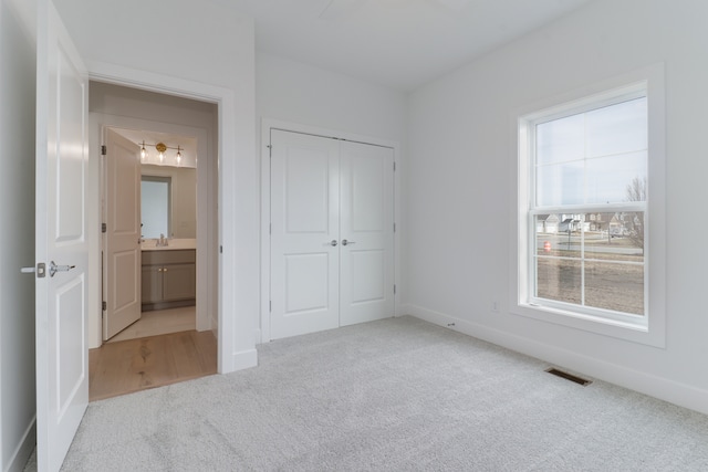 unfurnished bedroom with sink, a closet, ensuite bathroom, and light carpet