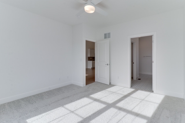 unfurnished bedroom with light carpet, a walk in closet, ceiling fan, and a closet