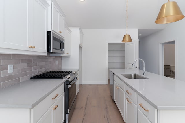 kitchen featuring a kitchen island with sink, decorative light fixtures, sink, appliances with stainless steel finishes, and white cabinets