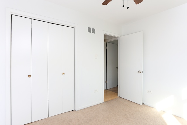 unfurnished bedroom with a closet, light colored carpet, and ceiling fan