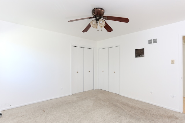 unfurnished bedroom with multiple closets, light colored carpet, and ceiling fan