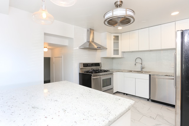 kitchen with wall chimney range hood, white cabinets, appliances with stainless steel finishes, pendant lighting, and sink