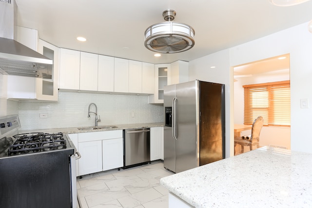 kitchen featuring wall chimney range hood, appliances with stainless steel finishes, sink, backsplash, and white cabinets