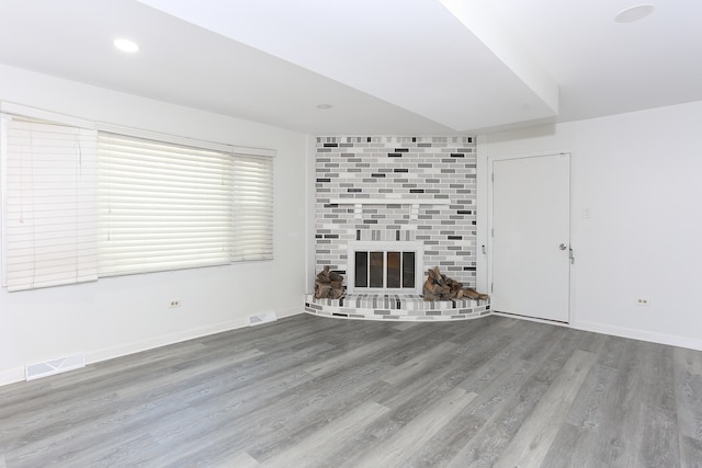 unfurnished living room featuring wood-type flooring and a brick fireplace