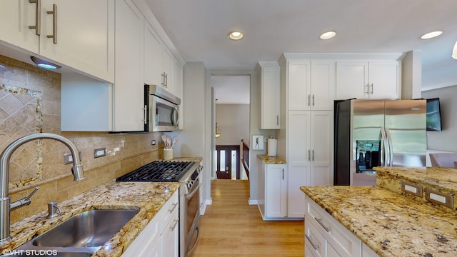 kitchen featuring light wood-type flooring, appliances with stainless steel finishes, white cabinetry, and decorative backsplash