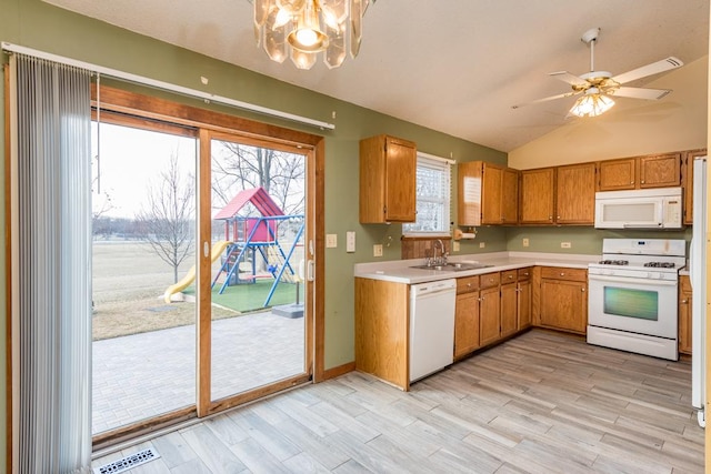 kitchen with white appliances, ceiling fan with notable chandelier, sink, vaulted ceiling, and light hardwood / wood-style flooring