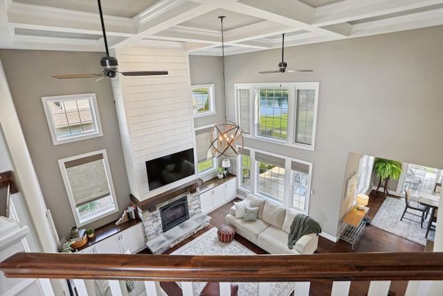 living room featuring beamed ceiling, a stone fireplace, and coffered ceiling