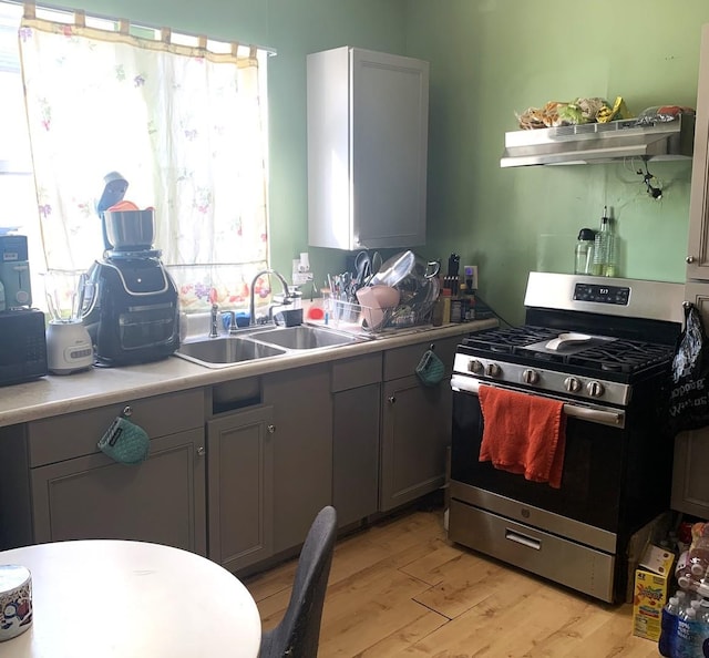 kitchen with light countertops, stainless steel range with gas stovetop, a sink, and light wood-style floors