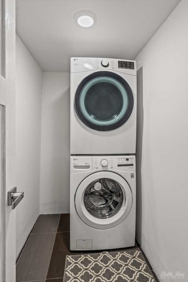 laundry area featuring dark tile patterned flooring and stacked washer and clothes dryer