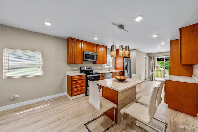 kitchen featuring sink, light wood-type flooring, appliances with stainless steel finishes, decorative light fixtures, and a kitchen bar