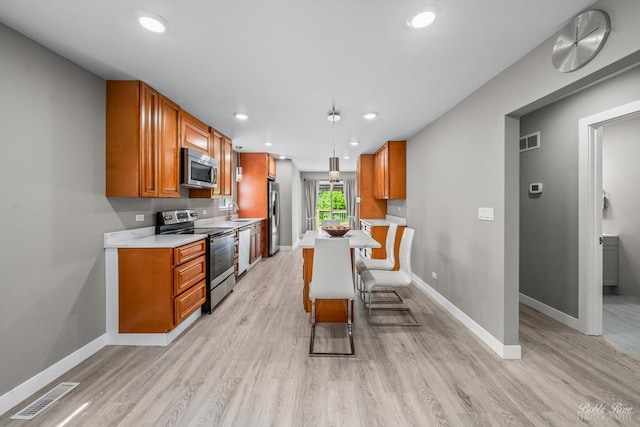 kitchen featuring decorative light fixtures, stainless steel appliances, a breakfast bar area, and light hardwood / wood-style floors