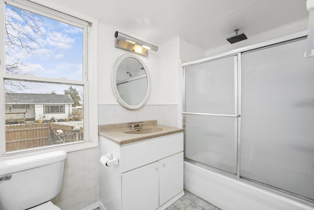 full bathroom with combined bath / shower with glass door, tile patterned floors, toilet, vanity, and tile walls