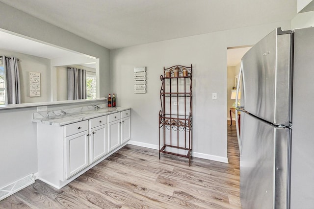 kitchen with stainless steel fridge, light stone countertops, light hardwood / wood-style flooring, kitchen peninsula, and white cabinets