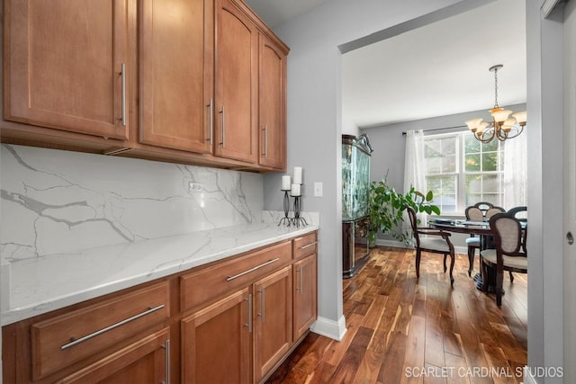 kitchen with pendant lighting, dark hardwood / wood-style floors, tasteful backsplash, light stone counters, and a chandelier