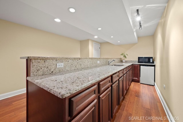 kitchen featuring dishwasher, light stone countertops, light wood-type flooring, and kitchen peninsula