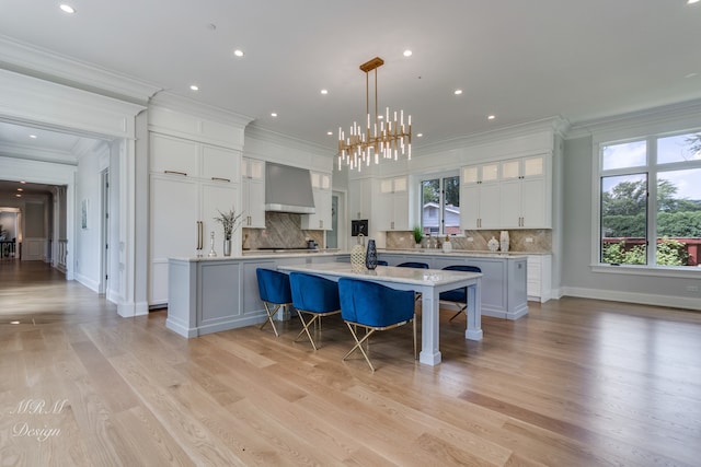 kitchen with white cabinets, decorative light fixtures, wall chimney range hood, and a kitchen island