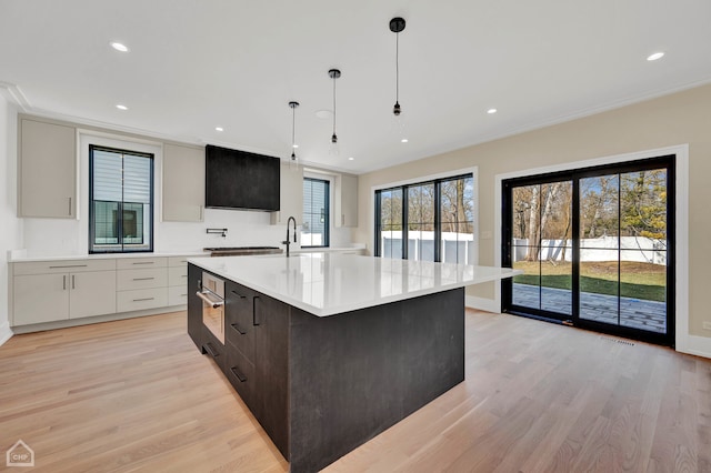 kitchen featuring an island with sink, white cabinets, plenty of natural light, and hanging light fixtures