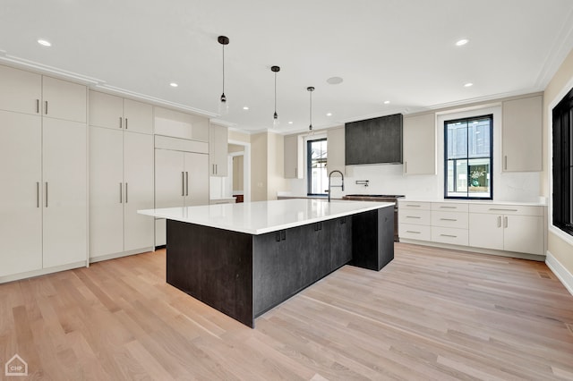 kitchen featuring a healthy amount of sunlight, light wood-type flooring, decorative light fixtures, and a large island with sink