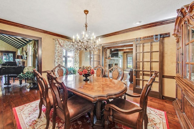 dining room with an inviting chandelier, a textured ceiling, ornamental molding, dark wood-type flooring, and a stone fireplace