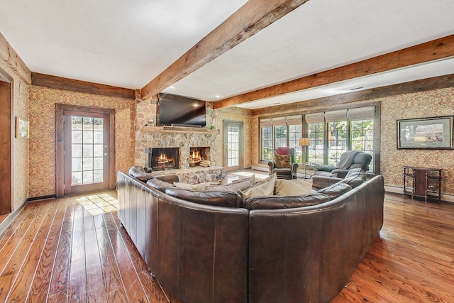 living room featuring a stone fireplace, beamed ceiling, plenty of natural light, and dark hardwood / wood-style floors