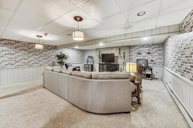 living room with a paneled ceiling, brick wall, a baseboard heating unit, and light carpet