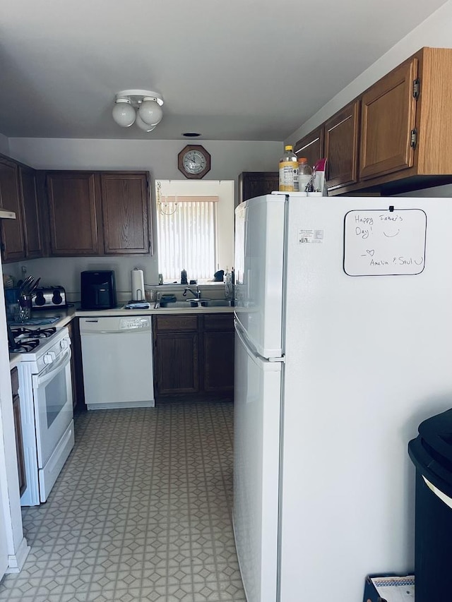 kitchen with light floors, light countertops, white appliances, and a sink