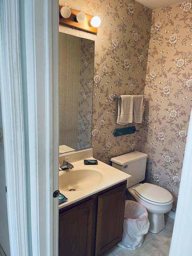 half bath with wallpapered walls, vanity, and toilet