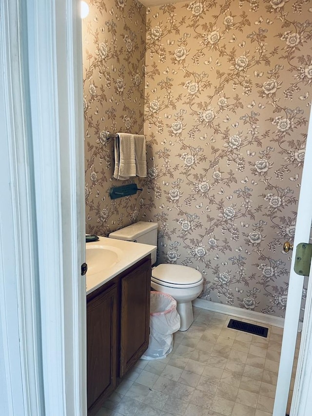 bathroom with wallpapered walls, visible vents, vanity, and baseboards