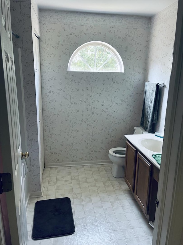 bathroom with baseboards, vanity, wallpapered walls, and toilet