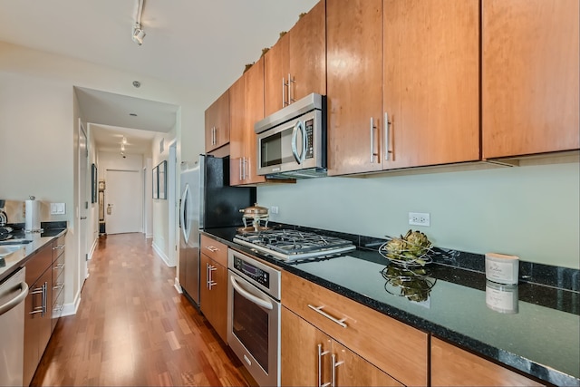 kitchen with appliances with stainless steel finishes, hardwood / wood-style floors, track lighting, and dark stone counters