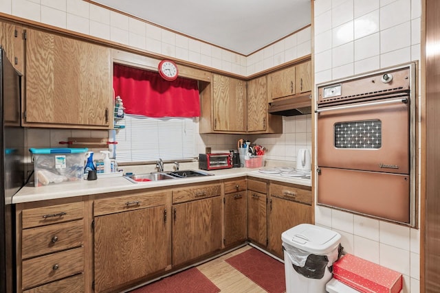 kitchen featuring backsplash, white stovetop, stainless steel oven, light hardwood / wood-style flooring, and sink