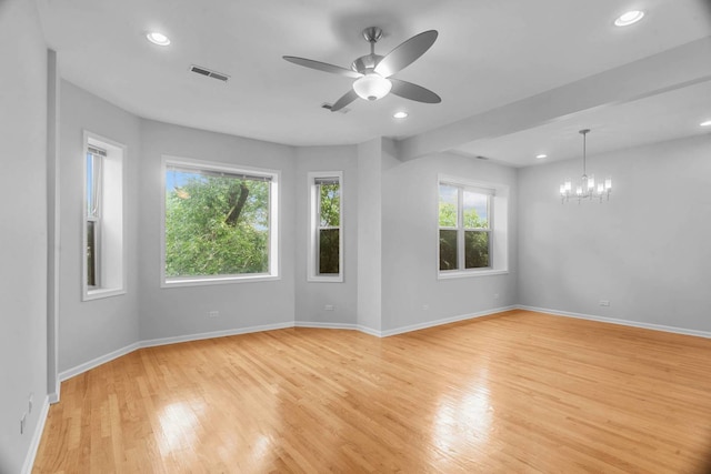 empty room with ceiling fan with notable chandelier and light hardwood / wood-style flooring