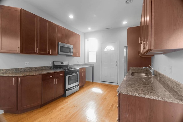 kitchen featuring dark stone countertops, appliances with stainless steel finishes, sink, and light hardwood / wood-style floors