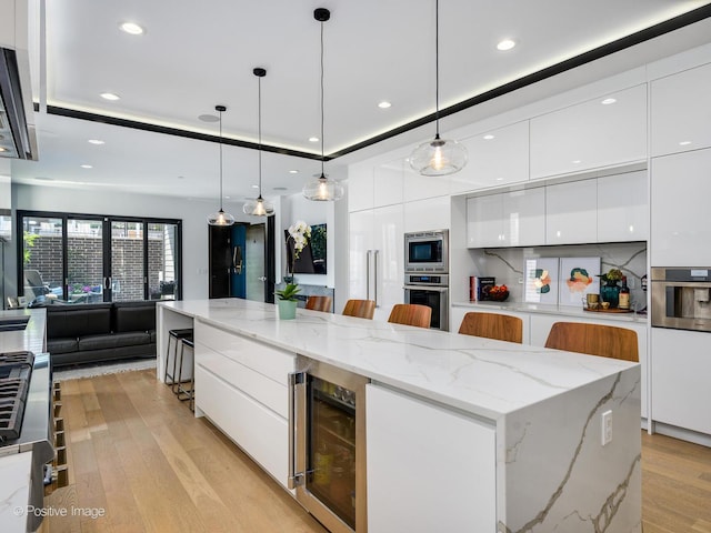 kitchen featuring a kitchen bar, beverage cooler, pendant lighting, stainless steel appliances, and a large island