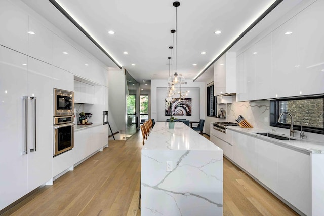 kitchen featuring a spacious island, sink, white cabinetry, hanging light fixtures, and appliances with stainless steel finishes