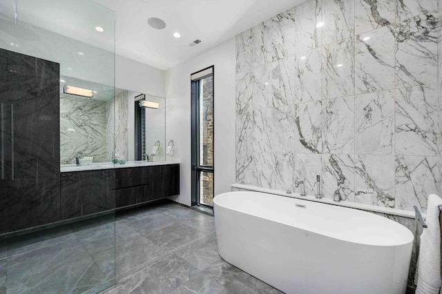 bathroom featuring vanity, a bath, and tile walls