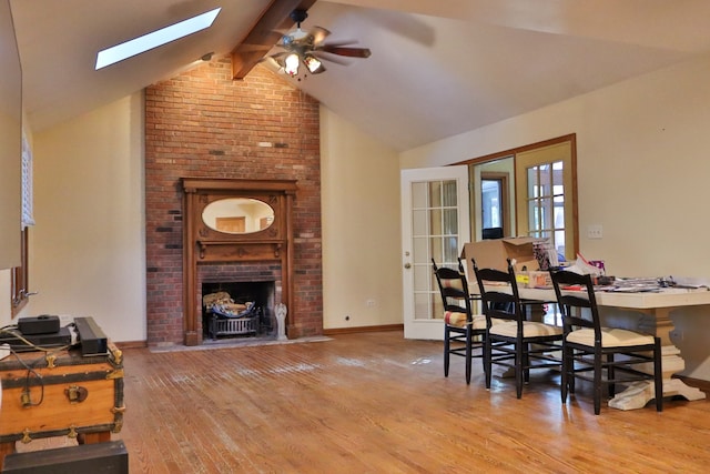 dining room featuring vaulted ceiling with skylight, ceiling fan, a brick fireplace, and hardwood / wood-style flooring