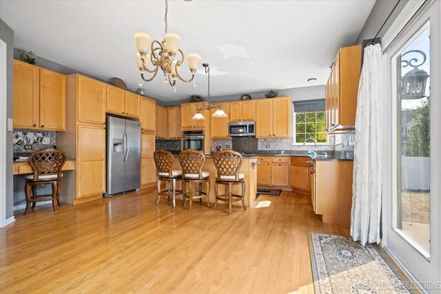 kitchen with a chandelier, a kitchen bar, a center island, appliances with stainless steel finishes, and light hardwood / wood-style floors