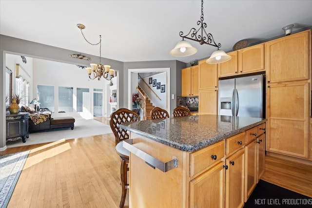 kitchen featuring hanging light fixtures, a center island, light wood-type flooring, dark stone counters, and stainless steel fridge with ice dispenser