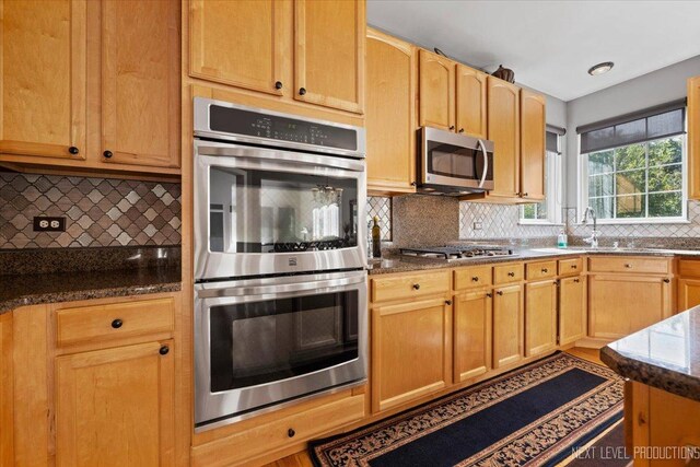 kitchen featuring appliances with stainless steel finishes, backsplash, dark stone counters, and sink