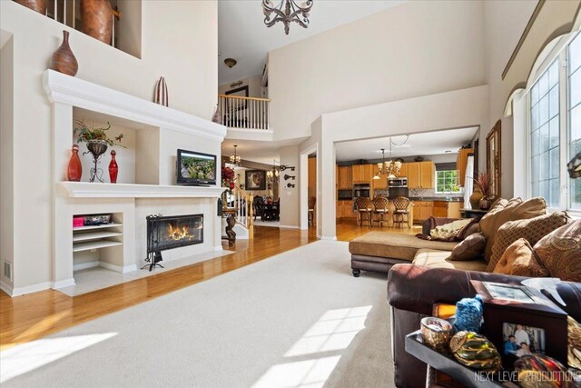 living room with light wood-type flooring, a notable chandelier, and a towering ceiling